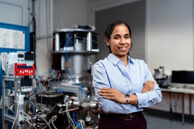 Aparajita Singha standing with arms crossed in a lab, surrounded by technical equipment.